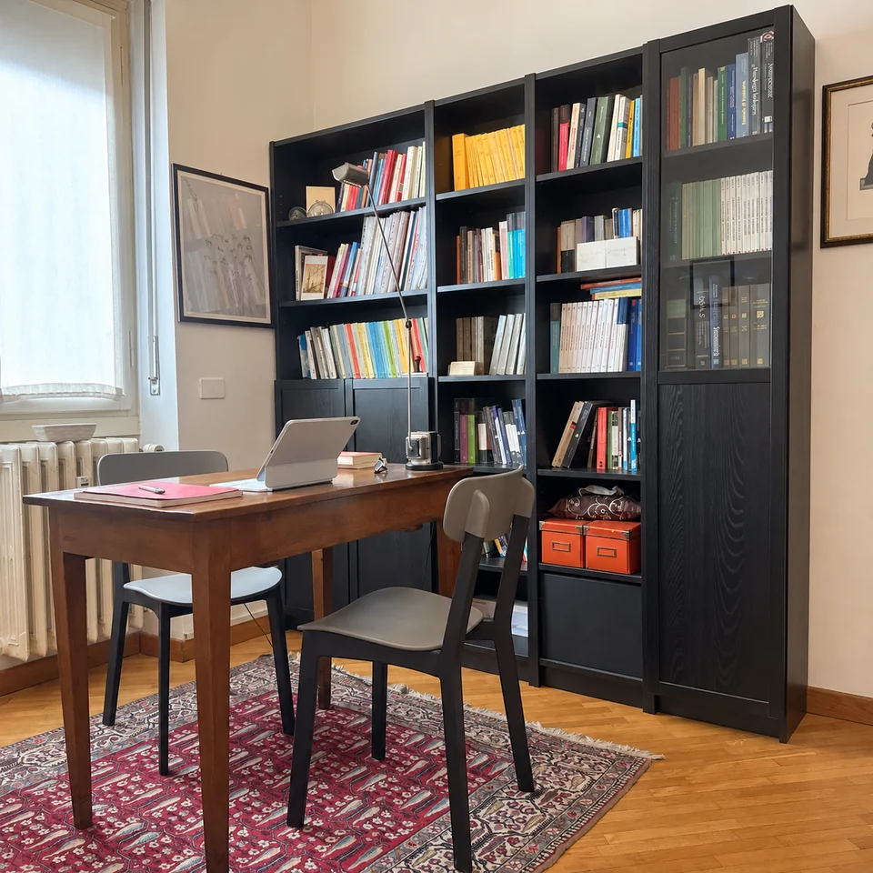 Scrivania con due sedute, libreria e luce dalla finestra nello studio di Daniele Colombo a Milano.
